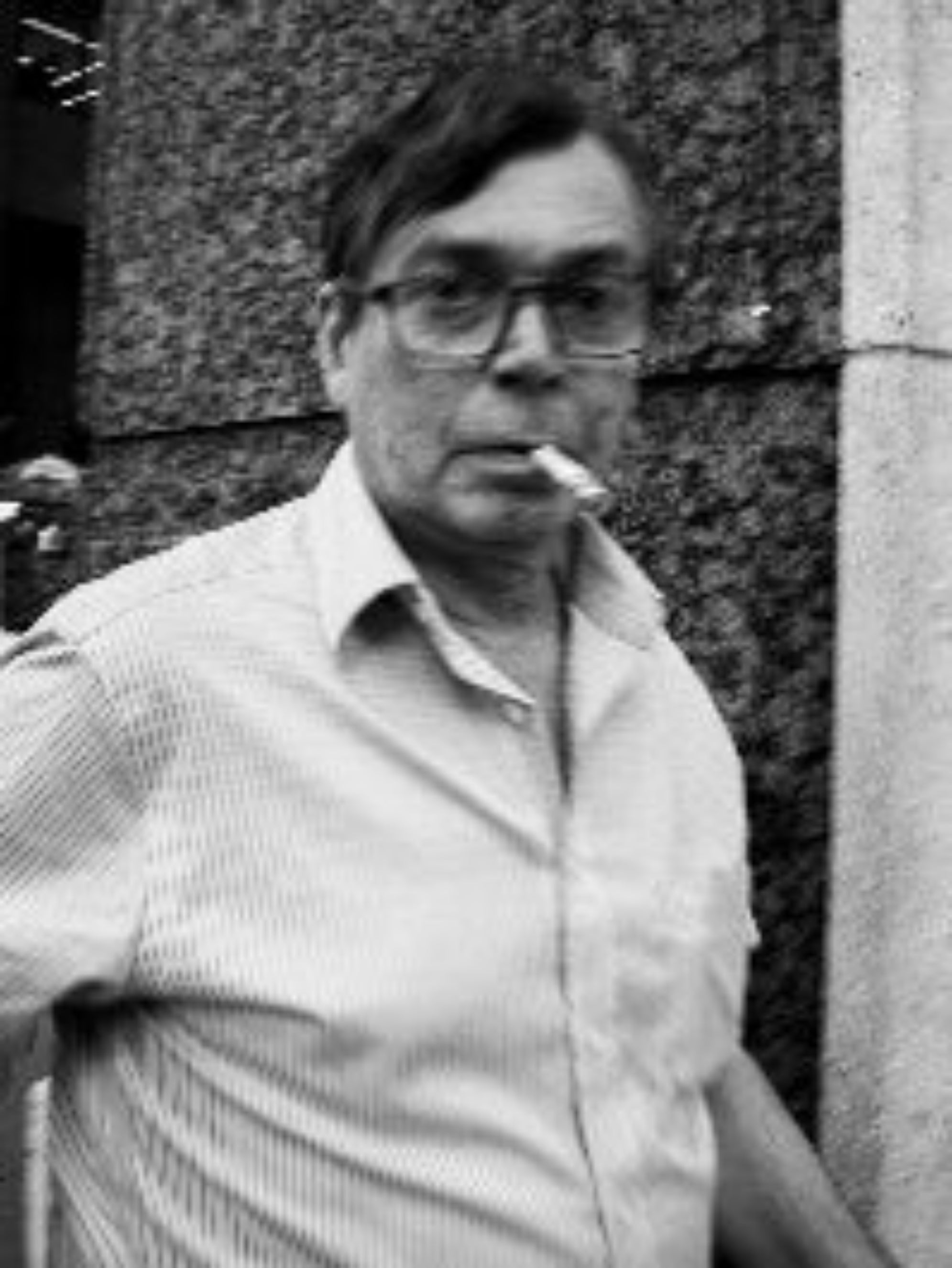 Black and white photo of a person smoking a cigarette outdoors.

